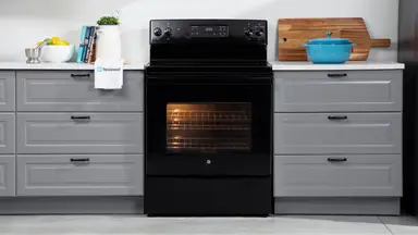 The GE JBS60DKBB electric range in black sits in a kitchen between grey cabinets.