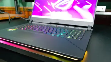 The Asus ROG Strix SCAR 17 (2023) open with a purple screensaver, on a desk
