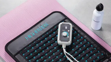 The Higher Dose Infrared PEMF Go Mat on a pink yoga mat, next to a Reviewed bottle.