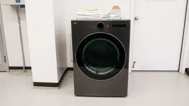 The dark steel-finished LG DLEX6700B dryer sits against a white wall next to a closed door in the Reviewed lab. Towels and a box of dyer sheets sit on the top of the machine.