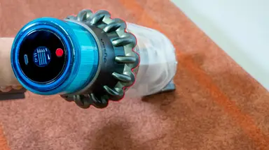 A hand holding the Dyson Gen5outsize with the LCD display screen showing while cleaning the floor