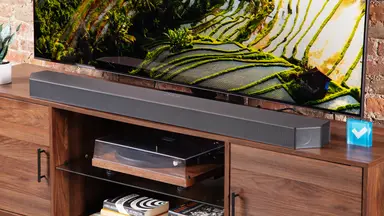 The Samsung HW-Q990C soundbar on a wooden home theater credenza in front of a TV.