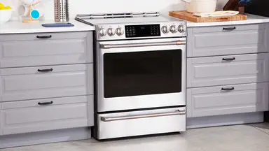 The Café CHS900P2MS range between two sets of grey cabinet drawers in a kitchen.