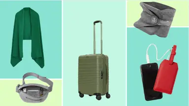A green shawl sweater, a grey fanny pack, an olive Beis carry-on roller, a grey Trtl neck pillow, and a red Calpak luggage tag and phone charger.