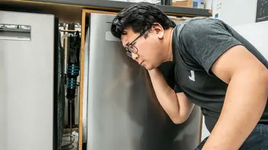 A person crouched down and listening closely to a dishwasher.
