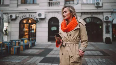 A woman wearing a trench coat with an orange sweater underneath.