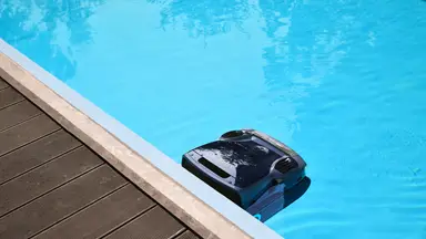 An Aiper robot pool cleaning floating on the water's surface at the edge of the pool