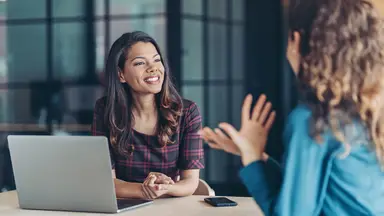 Two women in an office talking over an open laptop