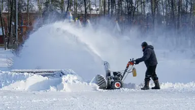 A person in winter wear puts their snow blower to good use following a heavy snowfall.