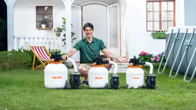 Pool owner in green shirt shown squatting behind three VEVOR sand filter pumps next to an above-ground pool, on green grass in front of a white house.