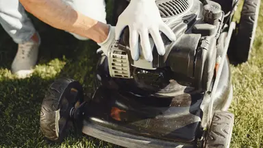 Person replacing blade on lawn mower while wearing gloves.