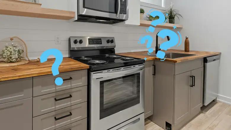 Modern kitchen with gray shaker cabinets, butcher block countertops, and a stainless steel electric kitchen range beneath a mounted microwave, illustrating what a kitchen range is in a compact contemporary cooking space.