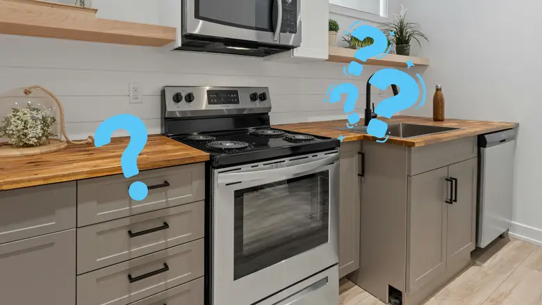 Modern kitchen with gray shaker cabinets, butcher block countertops, and a stainless steel electric kitchen range beneath a mounted microwave, illustrating what a kitchen range is in a compact contemporary cooking space.