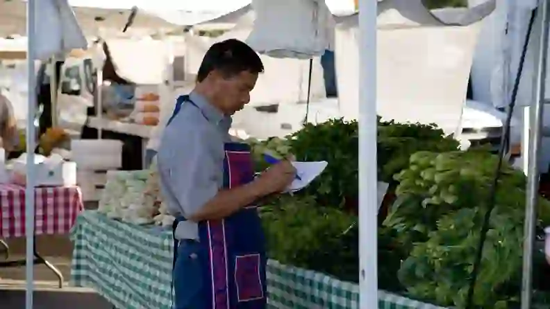 Farmer writing notes beside fresh produce stalls