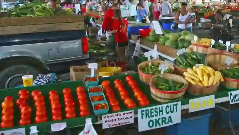 Market stand with tomatoes, squash, and "Fresh Cut Okra" signage