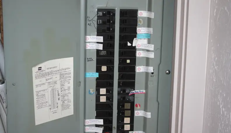 A standard green electrical panel stands open with all a home's circuits inside