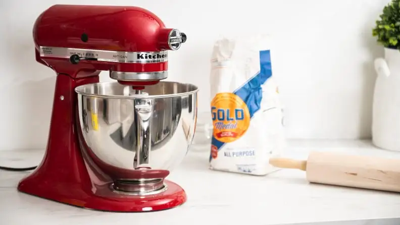 A red KitchenAid stand mixer on a kitchen counter next to flour and a rolling pin.