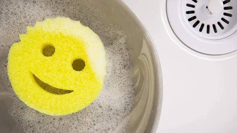 Smiley face sponges in pot in sink.