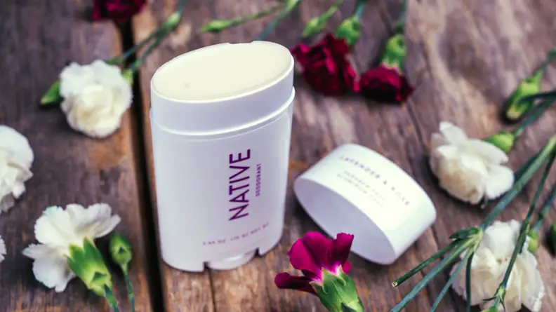 A stick of native deodorant surrounded by flowers