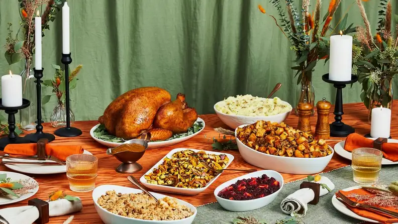 A Thanksgiving feast on an elaborately decorated table with sliced holiday turkey and various side dishes.