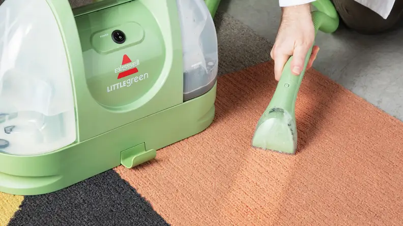 Eine Hand hält den Reinigungsschlauchkopf auf dem Teppich.