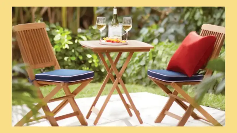 Wooden bistro set with matching blue cushions and one red pillow on a patio
