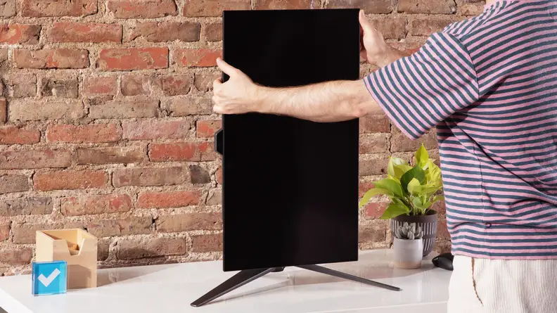 Person using hands to rotate the display vertically on the Asus ROG Swift OLED PG27AQDM desktop computer.
