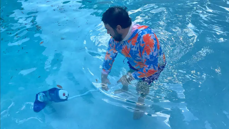 Person standing in pool while using the Pool Blaster pool vacuum to clean pool floor.