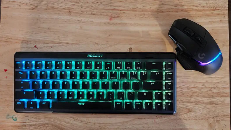 Roccat Vulcan II Mini Air keyboard with colorful LED backlit display next to computer mouse resting on top of hardwood surface.