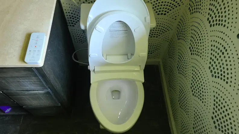 A toilet in a bathroom with the Alpha Bidet UX Pearl installed on it.