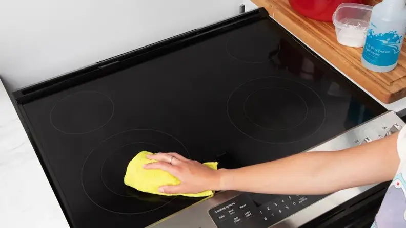 Person using yellow rag to polish and clean a glass stove top.