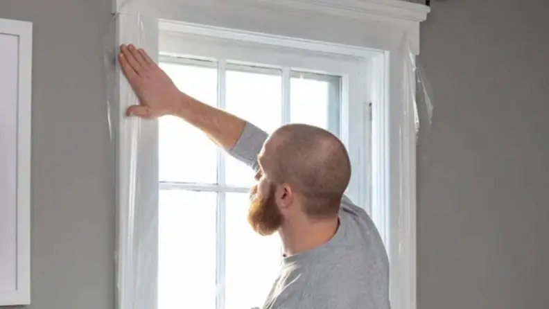 A man is affixing window cling to the interior of his home's window.