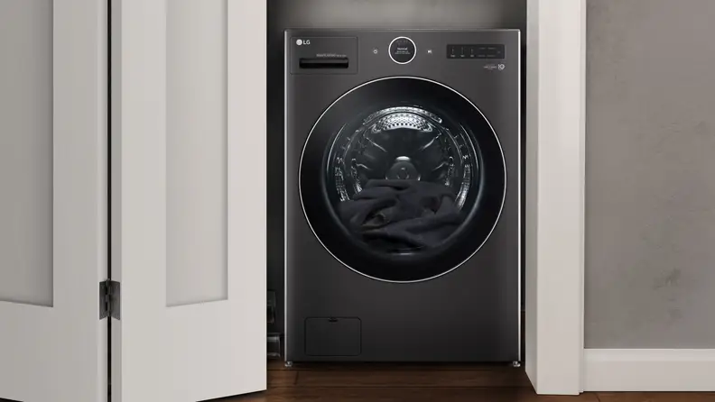 The LG Washer sits in a half-lit room next to a basket and chair.