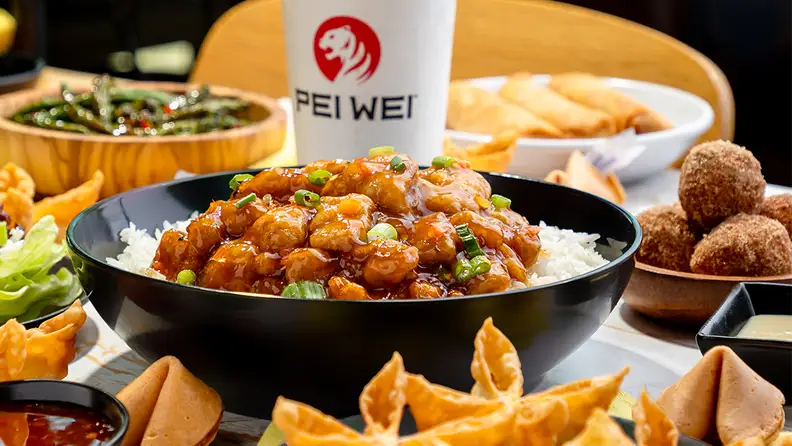 A bowl of beef noodle stir-fry next to a Pei Wei iced drink