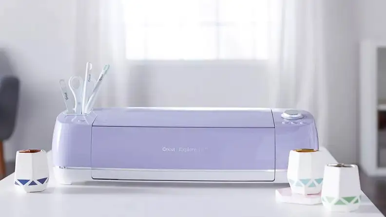 A purple Cricut machine sitting on a white desk in a sunny room.