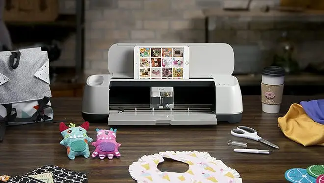 Cricut machine next to assorted crafts on table.
