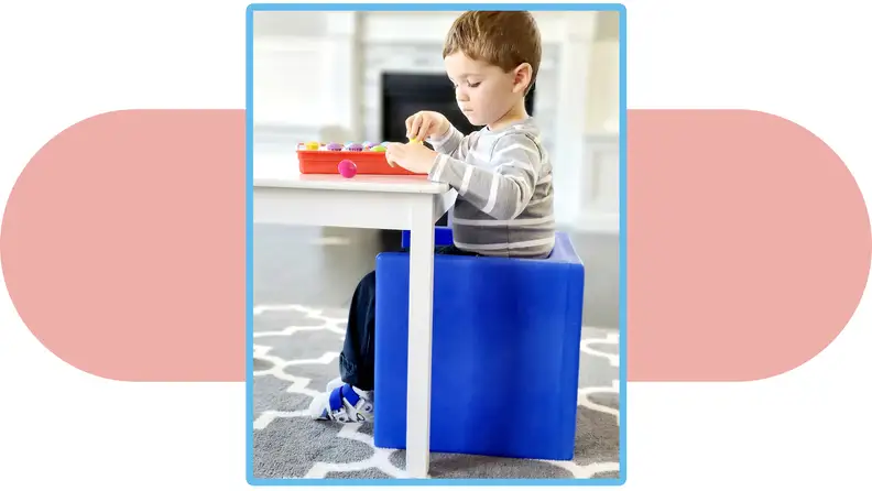 A child sits on a  cube chair and plays with a game on a table.