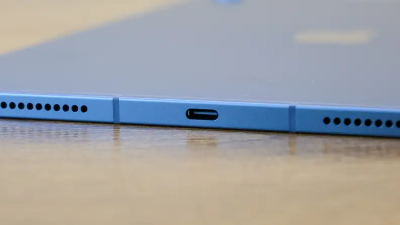 The blue Apple iPad 10 sits on a wooden desk with its thin profile and ports showing