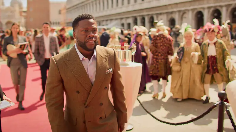 Kevin Hart dressed in a tan-colored suit walking on a red carpet in Venice.