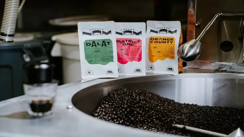 Three coffee bags standing beside a tray of roasted beans