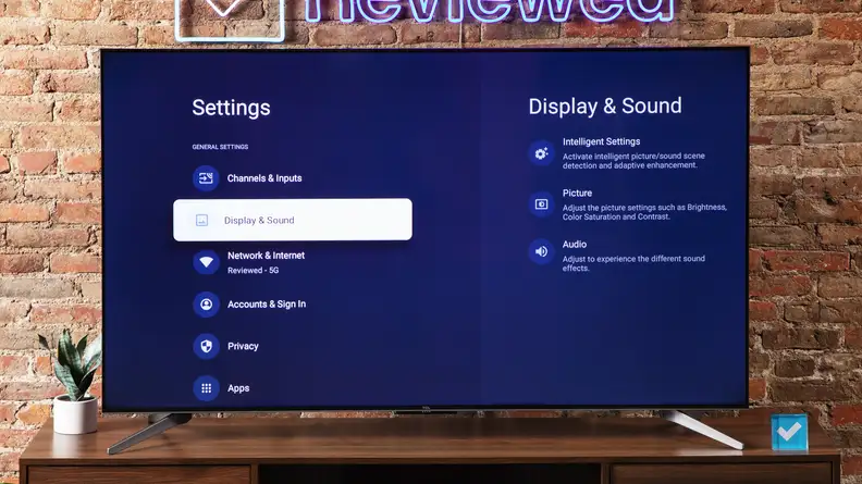 The TCL Q7 QLED TV on an entertainment center with a brick background.