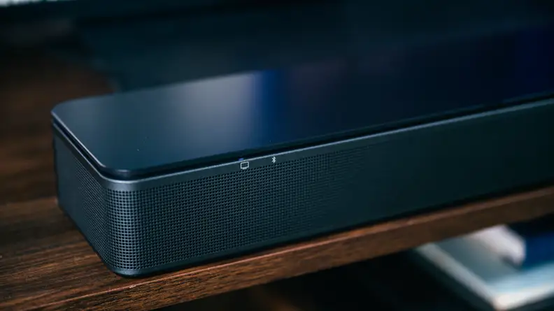 Indicator LEDs on the rim of the all-black TV Speaker, set on a rich brown wooden cabinet.