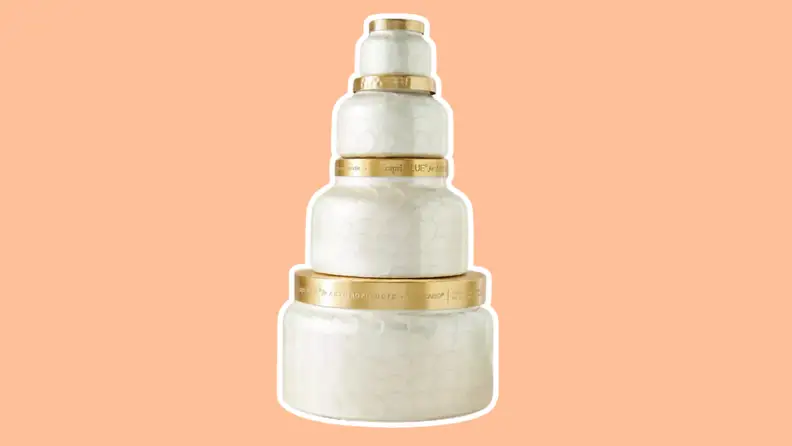 A stack of four Capri Blue candle jars in ascending order of sizes on an orange background.