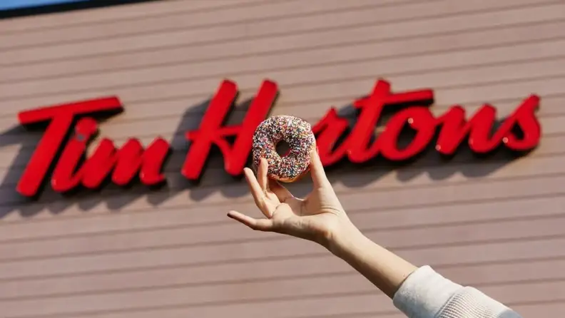 Hand holding a sprinkle donut in front of the Tim Hortons sign