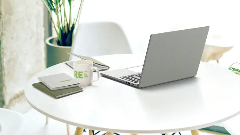 A light gray Acer Aspire Vero 16 sits on a white tabletop next to a coffee and notebooks.