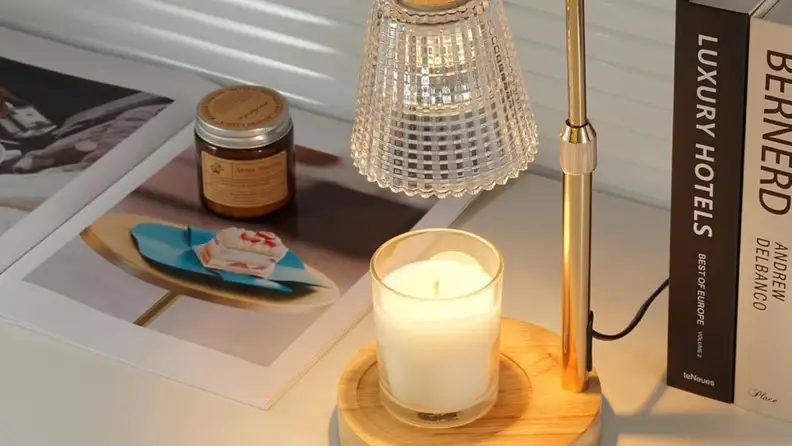 A rustic wood candle warmer sits with a white candle on a tabletop next to decorative books