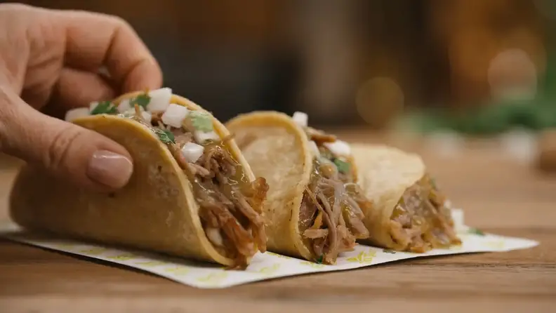 A hand reaching for shredded beef tacos topped with onion and cilantro
