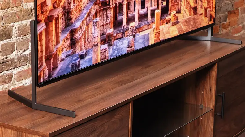A close-up of the feet attached to the Sony A95L QD-OLED TV while it's positioned in front of a brick wall