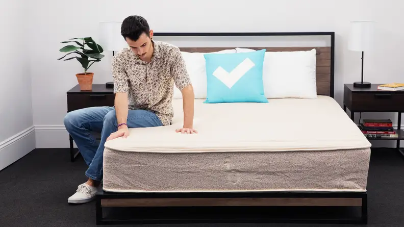 Tester Chris Panella sits on the Birch Natural Mattress while pressing his hands down to test firmness.
