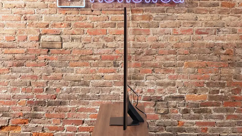 Side view of the QN90D's super thin screen and small base on top of wooden TV stand in front of brick wall.